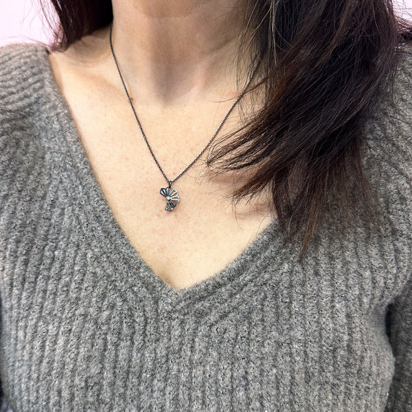 Karin Jacobson Jewelry's petite hyacinth fold necklace with tiny diamond - it shows an oxidized sterling silver flower-like pendant with a 2mm diamond set in 18k gold, on an oxidized sterling chain. photographed on a model.