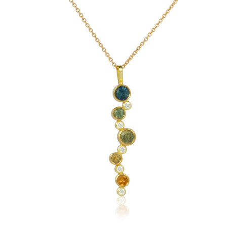 Shows an 18k yellow gold confetti necklace with various sizes of round Montana sapphires (in blue, teal, green, light yellow and dark yellow) and diamonds on a gold cable chain on a white background. close up photo.