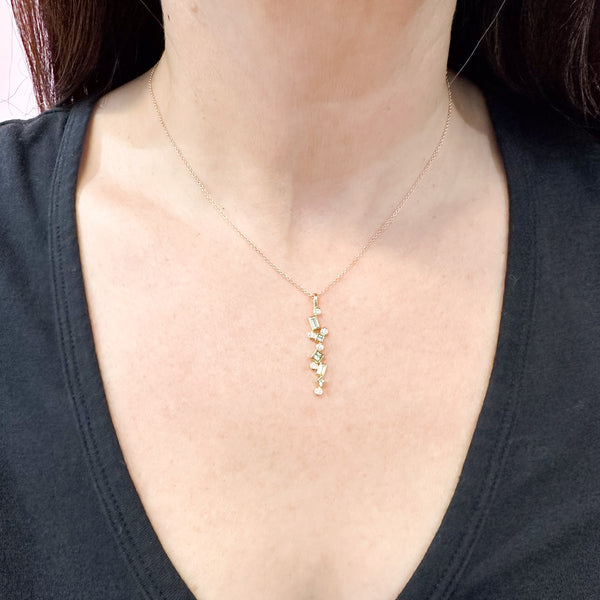 Shows an 18k yellow gold confetti necklace with various square, rectangle and round seafoam (pale green) tourmalines and diamonds, hanging from a gold cable chain on a model.