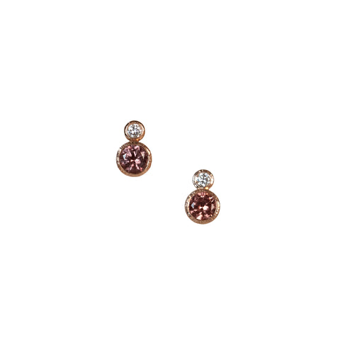 A pair of garnet and diamond studs earrings with round Malaya garnets and round recycled diamonds set in 14k rose gold.