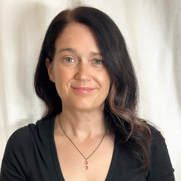 Photo of a woman wearing a vertical pendant with two Umba sapphires and a small diamond between them, set in recycled 18k yellow gold on an oxidized silver cable chain.