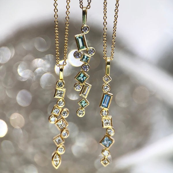 This photo shows three confetti pendants: on the left is all diamond, in the middle is seafoam tourmaline & diamond; and on the right is aquamarine and diamond. the photo has a sparkly gray background.