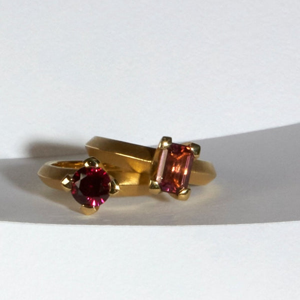 karin jacobson jewelry design - photo of two solitaires in fairmined 18k yellow gold. This grape garnet round prong set ring and the pink tourmaline emerald cut prong set ring.