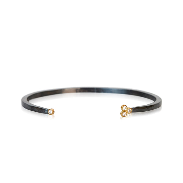 Oxidized silver cuff bracelet with one diamond on one end and a three-diamond cluster on the other, set in 18k yellow gold.