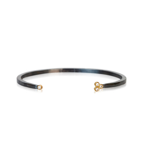 Oxidized silver cuff bracelet with one diamond on one end and a three-diamond cluster on the other, set in 18k yellow gold.