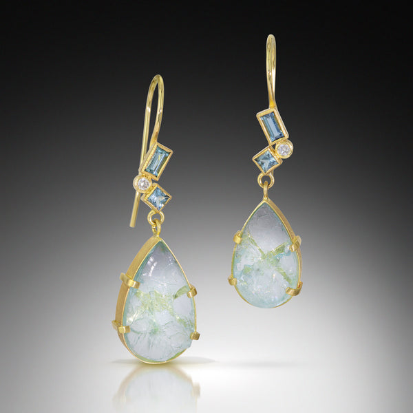 Photo of karin jacobson jewelry design pear shaped aquamarine and diamond earrings in 18k yellow gold. The pear shaped rough aquamarines are set in a hand fabricated 18k yellow gold setting with a cluster of faceted aquamarines and post consumer recycled diamonds on the bail. These earrings have french wires. Shown on black background.