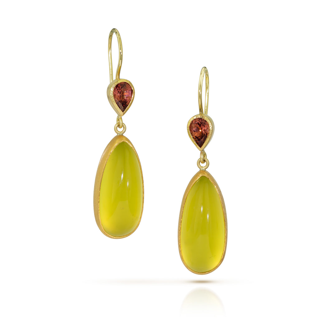 Pair of drop earrings with pear-shaped orange Umba garnets above elongated yellow-green vesuvianite cabochons, set in matte 18k yellow gold, on a light background.