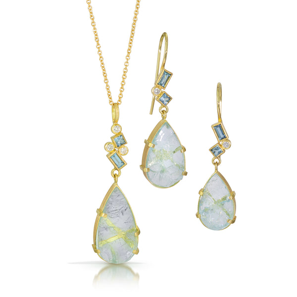 Photo of karin jacobson jewelry design pear shaped aquamarine and diamond necklace 18k yellow gold. The pear shaped rough aquamarine is in a hand fabricated 18k yellow gold setting with a cluster of faceted square and baguette aquamarines & round diamonds on the bail. Shown hanging on an 18k yellow gold cable chain. Shown with matching earrings