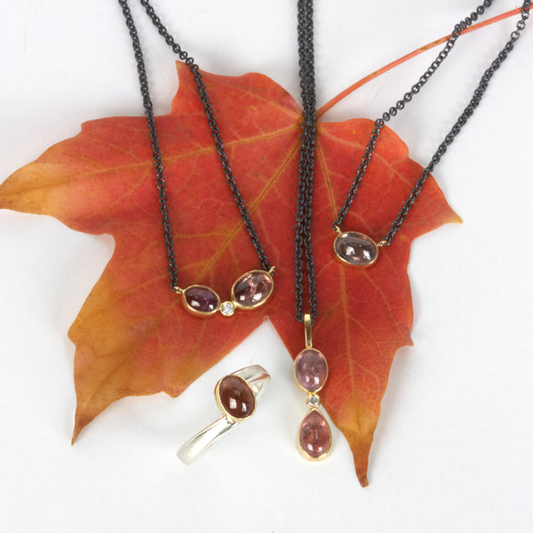 Small oval Umba sapphire pendant in recycled 18k yellow gold on an oxidized silver cable chain. Shown with two other matching pendants and a matching ring and autumn leaves.