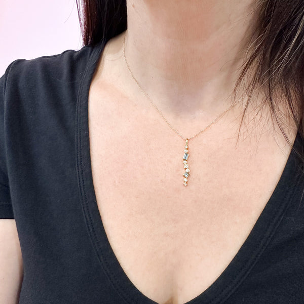 Shows an 18k yellow gold confetti necklace with various square, rectangle and round aquamarines and diamonds, hanging from a gold cable chain on a model.