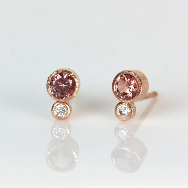 A pair of garnet and diamond studs earrings with round Malaya garnets and round recycled diamonds set in 14k rose gold.