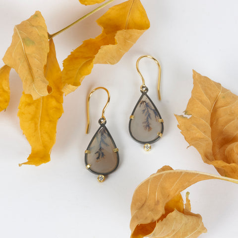 Pair of pear-shaped dendritic agate drop earrings in oxidized sterling silver with 18k yellow gold prongs, each accented with a small diamond below and finished with 18k gold French wires. Shown with yellow autum leaves.