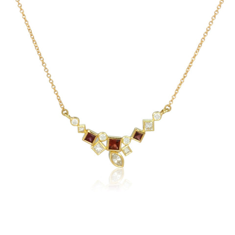 Shows an 18k yellow gold confetti necklace with various square, rectangle and marquise (canoe shaped) garnets (rusty reds) and diamonds, hanging from a gold cable chain on a white background. Close up shot