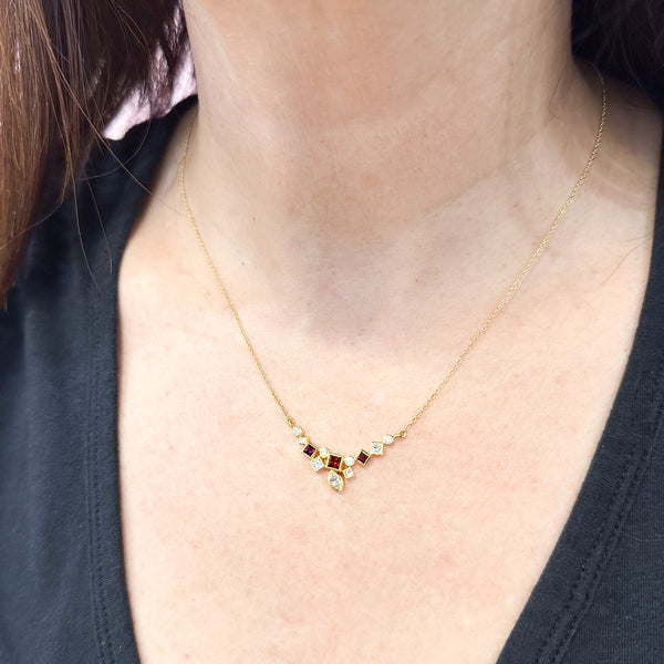 Shows an 18k yellow gold confetti necklace with various square, rectangle and marquise (canoe shaped) garnets (rusty reds) and diamonds, hanging from a gold cable chain on a model.