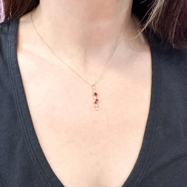 Shows an 18k yellow gold confetti necklace with various square, rectangle and round grape garnets (pinkish red) and diamonds, hanging from a gold cable chain on a model.