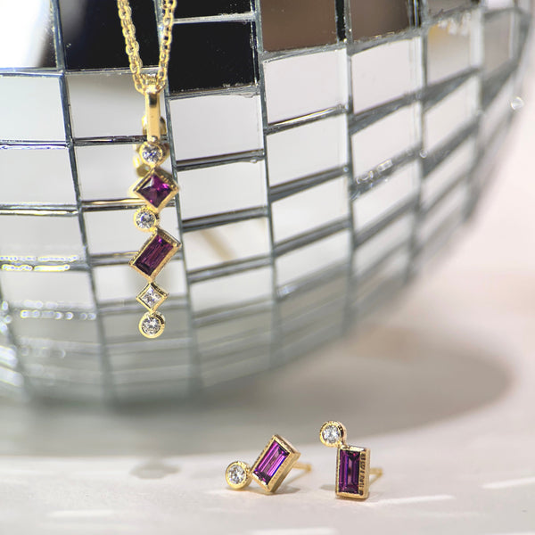 Shows a necklace and pair of studs earrings - both with various square and round garnets and diamonds set in 18k gold) with a little disco ball in the background.