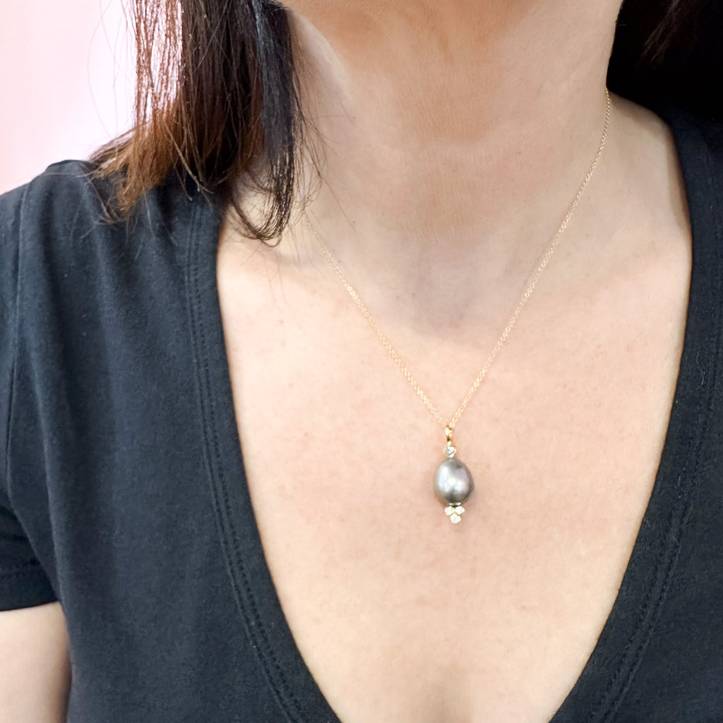 This photo shows an 18k yellow gold confetti necklace with a gray pearl - it has a 3mm gray sapphire on top and a cluster of three diamonds on the bottom - hanging from a gold cable chain, shown on a model.
