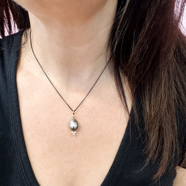 This photo shows an 18k yellow gold confetti necklace with a gray pearl - it has a 3mm gray sapphire on top and a cluster of three diamonds on the bottom - hanging from an oxidized sterling cable chain, shown on a model.