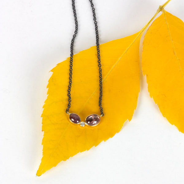 Necklace with two oval Umba sapphires and a small diamond between them, set in recycled 18k yellow gold on an oxidized silver cable chain. Shown on autumn leaves