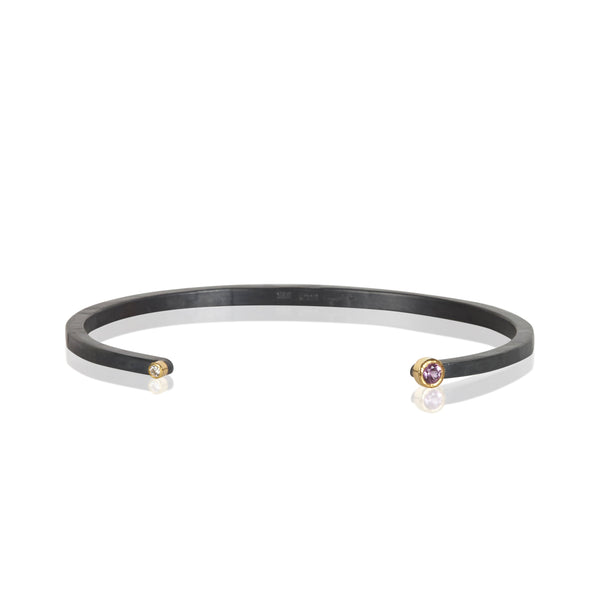 Oxidized sterling silver cuff bracelet with a diamond on one end and a small round bright pink sapphire on the other, both set in 18k yellow gold.