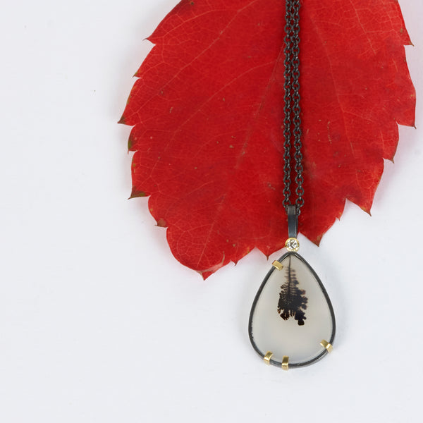 Pear-shaped dendritic agate pendant in oxidized sterling silver with 18k yellow gold prongs and a small diamond accent above, shown on an oxidized silver cable chain. Shown with red autum leaf.