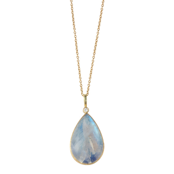 Photo of karin jacobson jewelry design pear shaped rainbow moonstone cabochon and diamond necklace in sterling silver, 22k & 18k yellow gold. It has a large pear moonstone that has inclusions and glows blue, with one diamond at the top of the pendant. Shown hanging from a gold chain.