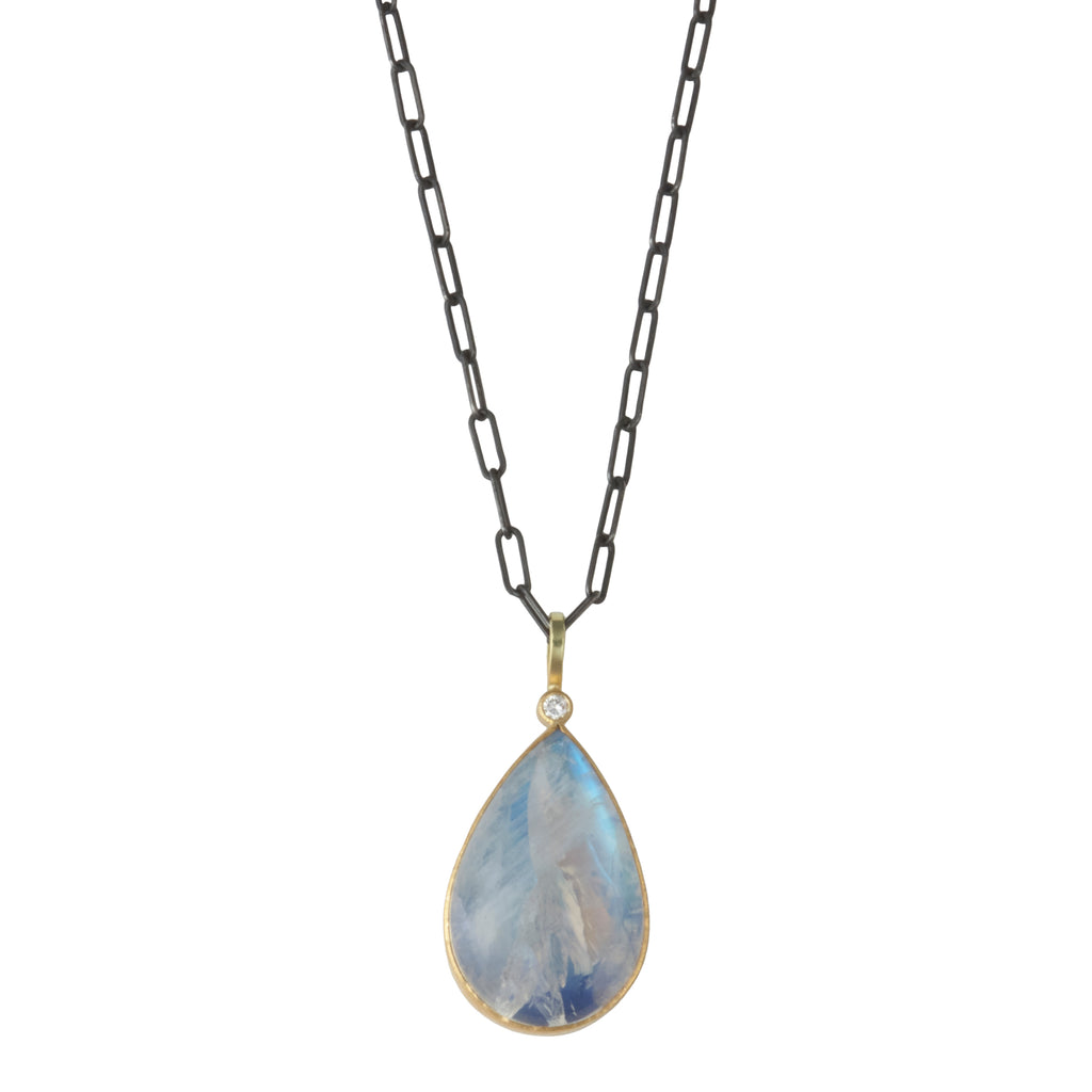Photo of karin jacobson jewelry design pear shaped rainbow moonstone cabochon and diamond necklace in sterling silver, 22k & 18k yellow gold. It has a large pear moonstone that has inclusions and glows blue, with one diamond at the top of the pendant. Shown hanging from an oxidized silver chain.