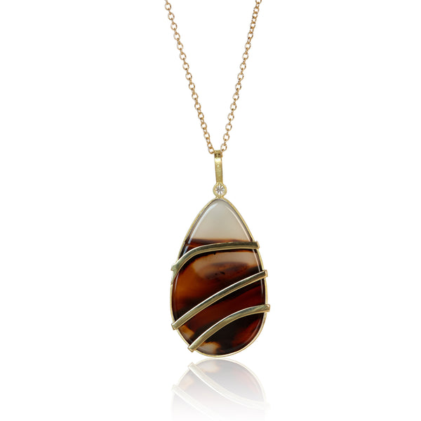 Back of teardrop-shaped Montana agate pendant with custom gold wirework following the stone’s layered brown and white patterns.
