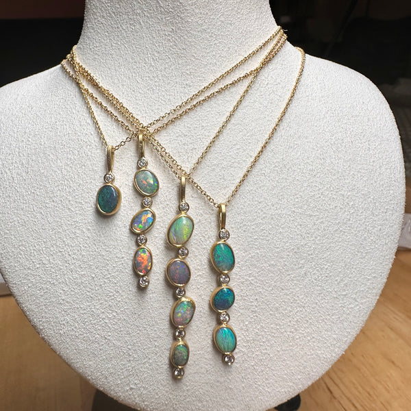 Karin Jacobson jewelry collection of 4 opal necklaces with opals and diamonds in 18k & 22k gold and sterling silver back, on 18k gold chain. shown on a jewelry prop.