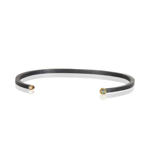 Oxidized sterling silver cuff bracelet with a diamond on one end and a small round bi-color sapphire on the other, both set in 18k yellow gold.