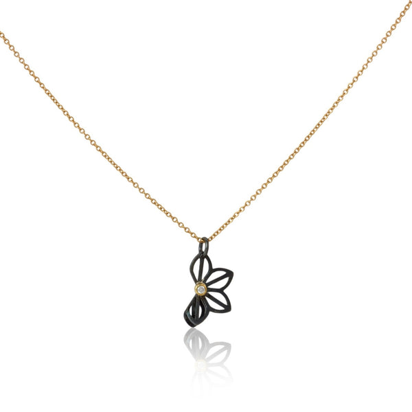 Karin Jacobson Jewelry's petite anise fold necklace with tiny diamond - it shows an oxidized sterling silver flower-like pendant with a 2mm diamond set in 18k gold, on an 18k gold chain. photographed on white.