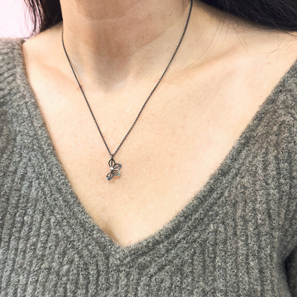 Karin Jacobson Jewelry's petite anise fold necklace with tiny diamond - it shows an oxidized sterling silver flower-like pendant with a 2mm diamond set in 18k gold, on an oxidized sterling chain. photographed on a model.