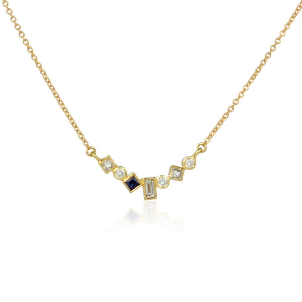 Shows an 18k yellow gold confetti necklace with various square, rectangle and round diamonds with one dark blue square sapphire, hanging from a gold cable chain on a white background. Close up shot