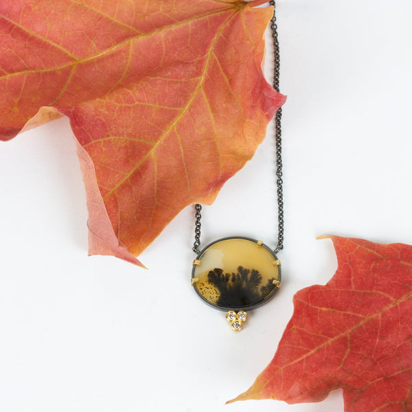 Round dendritic agate pendant in oxidized sterling silver with 18k yellow gold prongs and a cluster of three small diamonds below, shown on an oxidized silver cable chain. Shown with autumn leaves.