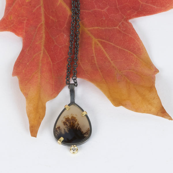 Small pear-shaped dendritic agate pendant in oxidized sterling silver with 18k yellow gold prongs and a single diamond accent below, shown on an oxidized silver cable chain. Shown next to an autumn leaf