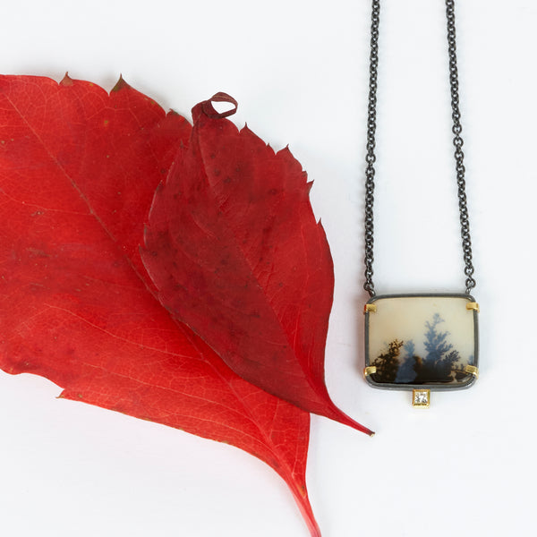 Rectangular dendritic agate pendant in oxidized sterling silver with 18k yellow gold prongs and a small diamond accent below, shown on an oxidized silver cable chain. shown with red leaves
