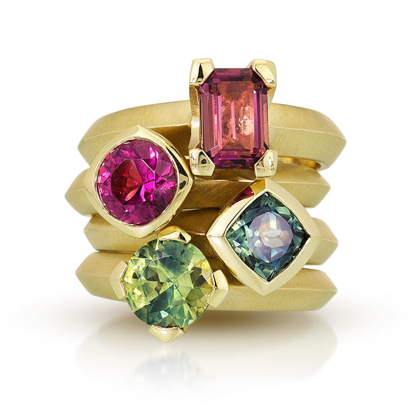 Photo of stack of four fairmined 18k yellow gold solitaires with Malawi pink tourmaline emerald cut on top; Malawi pink tourmaline round cut second from top; Australian cushion cut teal sapphire second from bottom and Australian green sapphires by karin jacobson jewelry design